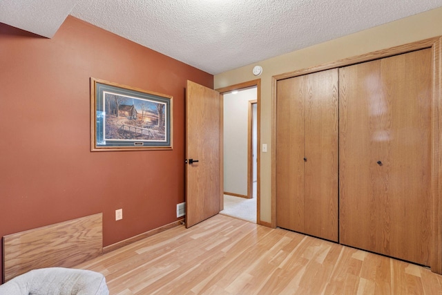 unfurnished bedroom with visible vents, a textured ceiling, a closet, light wood-style floors, and baseboards