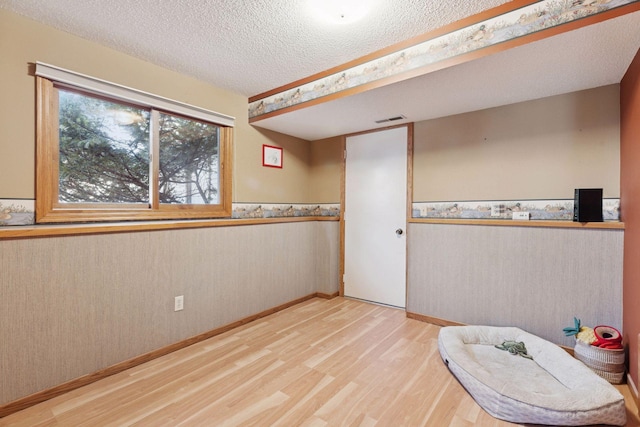 empty room featuring a textured ceiling, wood finished floors, visible vents, and wainscoting