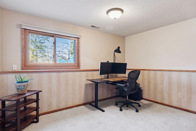 carpeted home office featuring visible vents, a textured ceiling, wallpapered walls, and baseboards