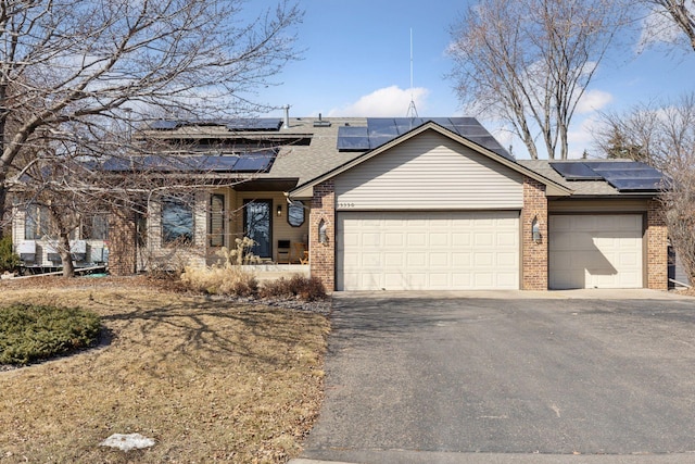 view of front of house with driveway, roof mounted solar panels, roof with shingles, an attached garage, and brick siding