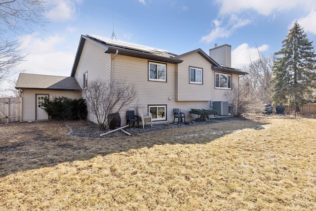 back of property featuring central air condition unit, a lawn, a chimney, and fence