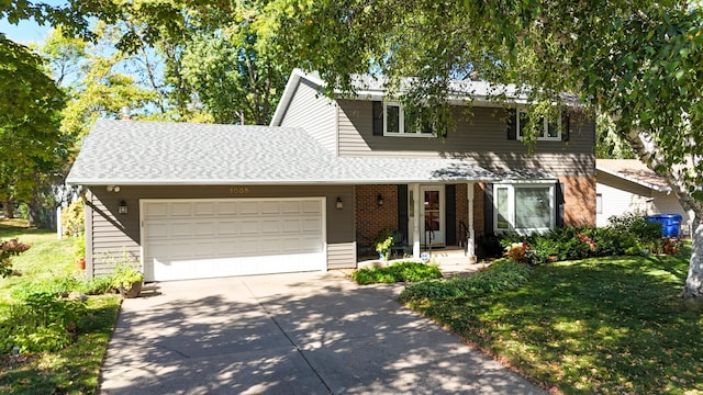 traditional-style house featuring a front yard, driveway, an attached garage, a shingled roof, and brick siding