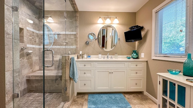 full bath with vanity, a textured wall, a stall shower, and baseboards