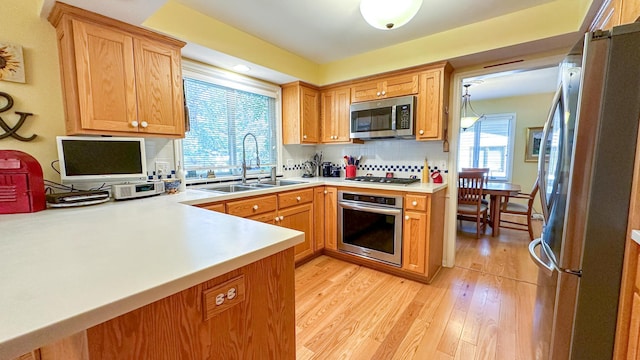 kitchen featuring light wood finished floors, backsplash, light countertops, stainless steel appliances, and a sink