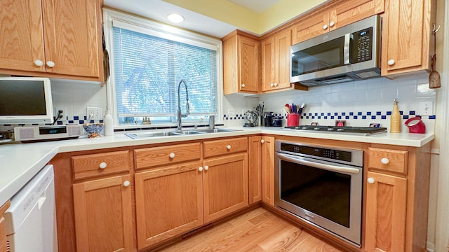 kitchen featuring light wood finished floors, light countertops, decorative backsplash, appliances with stainless steel finishes, and a sink