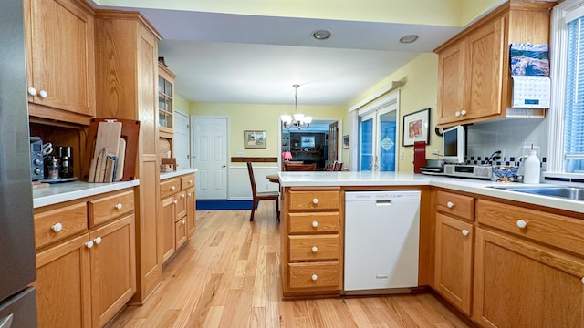 kitchen featuring a peninsula, white dishwasher, light countertops, light wood-style floors, and a chandelier