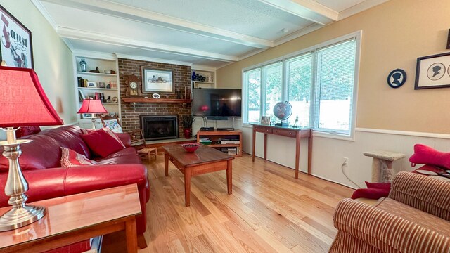 living room with beamed ceiling, built in shelves, a fireplace, and light wood-type flooring