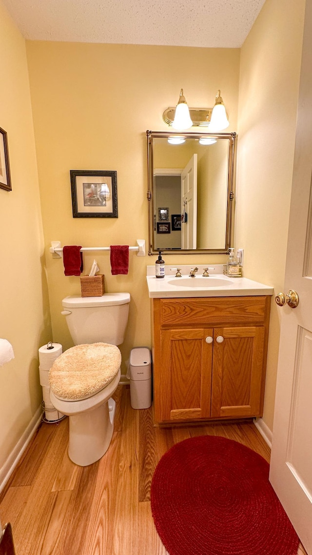 bathroom with vanity, wood finished floors, baseboards, a textured ceiling, and toilet