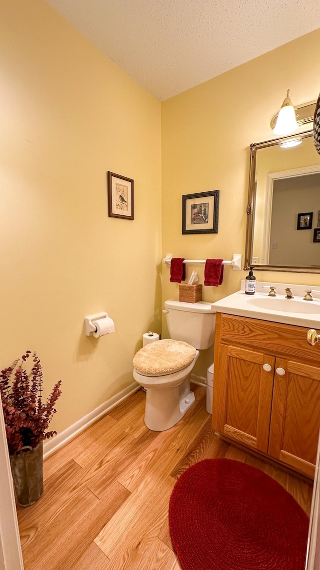 half bathroom featuring vanity, wood finished floors, baseboards, a textured ceiling, and toilet