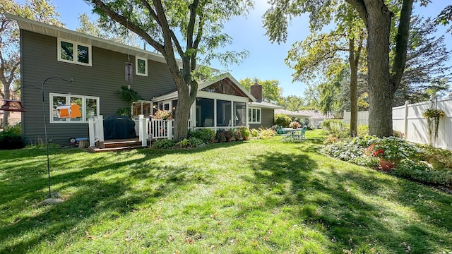 back of house featuring a chimney, fence, a yard, and a sunroom