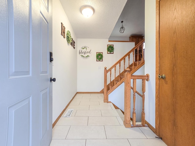 foyer entrance featuring stairway, baseboards, visible vents, light tile patterned flooring, and a textured ceiling