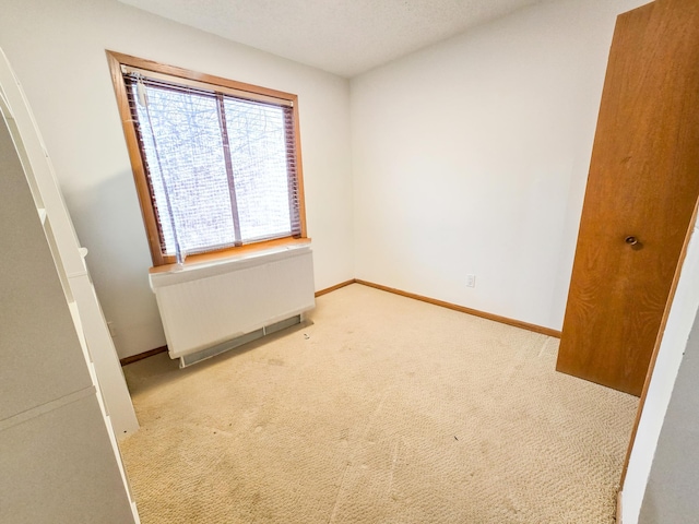 carpeted empty room featuring baseboards and radiator