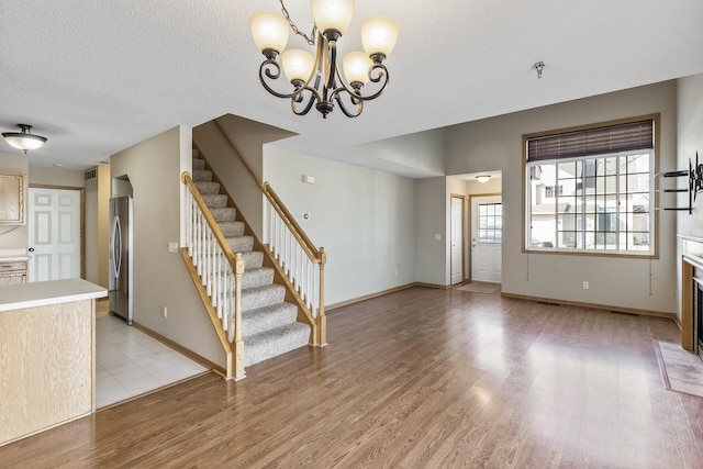 unfurnished living room featuring baseboards, a chandelier, stairway, light wood-type flooring, and a textured ceiling