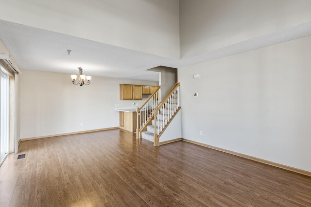 empty room featuring stairs, an inviting chandelier, wood finished floors, and visible vents