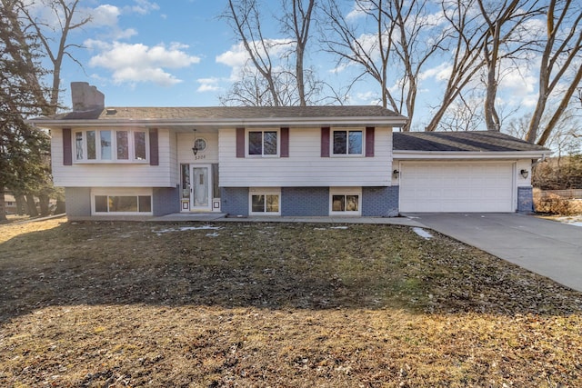 bi-level home featuring brick siding, an attached garage, a chimney, and driveway