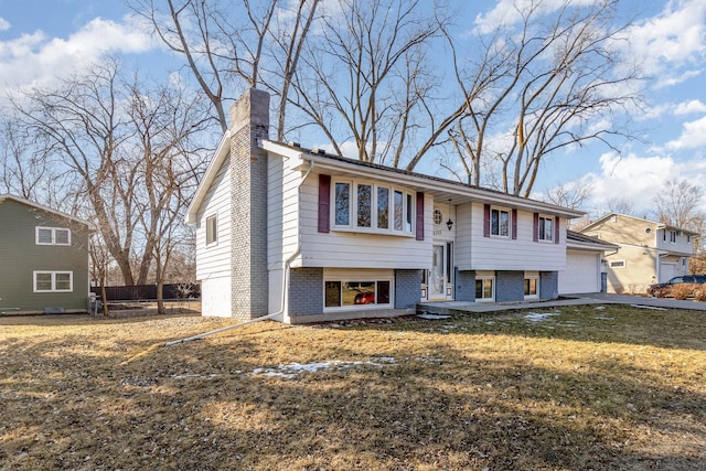 raised ranch with a front yard, fence, a chimney, a garage, and brick siding