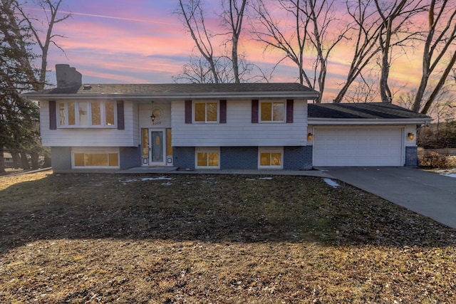 split foyer home featuring brick siding, an attached garage, a chimney, and driveway