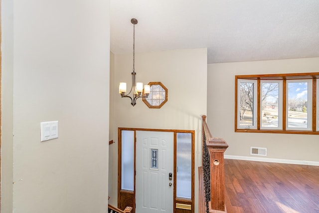 foyer entrance featuring a notable chandelier, visible vents, baseboards, and wood finished floors