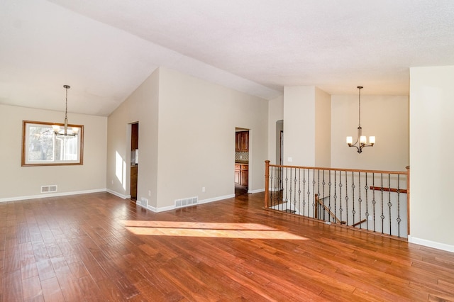 empty room with a notable chandelier, visible vents, and wood finished floors