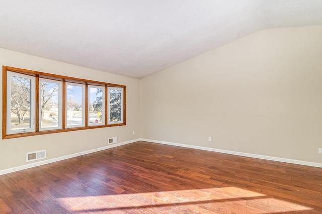 empty room with dark wood-style floors, visible vents, baseboards, and lofted ceiling