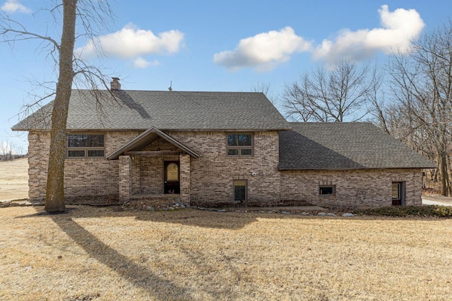 view of front facade with a front lawn, brick siding, a chimney, and a shingled roof