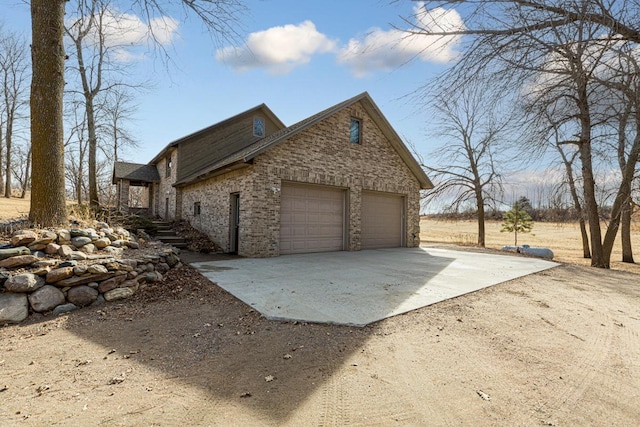 view of side of home featuring brick siding, an attached garage, and concrete driveway