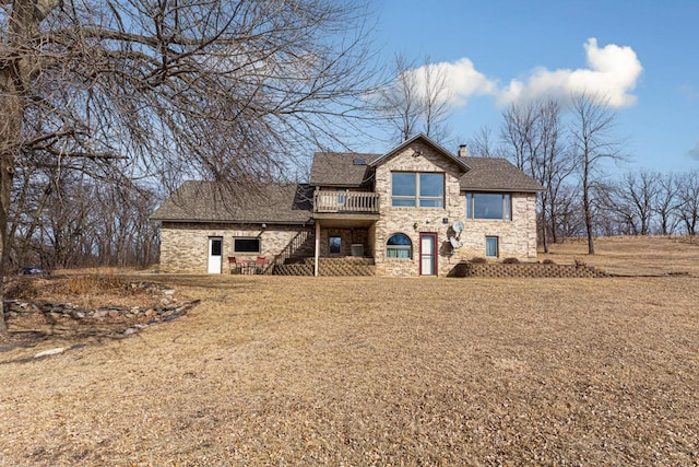 view of front of home with a front lawn, a balcony, stone siding, and a chimney