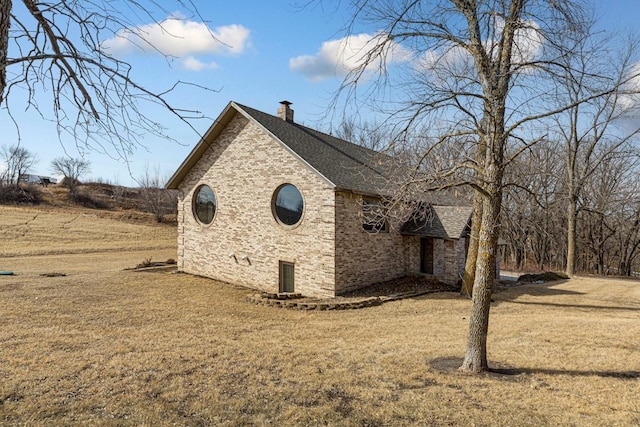 view of side of home with brick siding, a lawn, a chimney, and roof with shingles