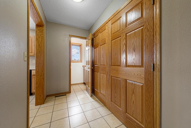 doorway to outside with light tile patterned flooring, a textured wall, baseboards, and a textured ceiling