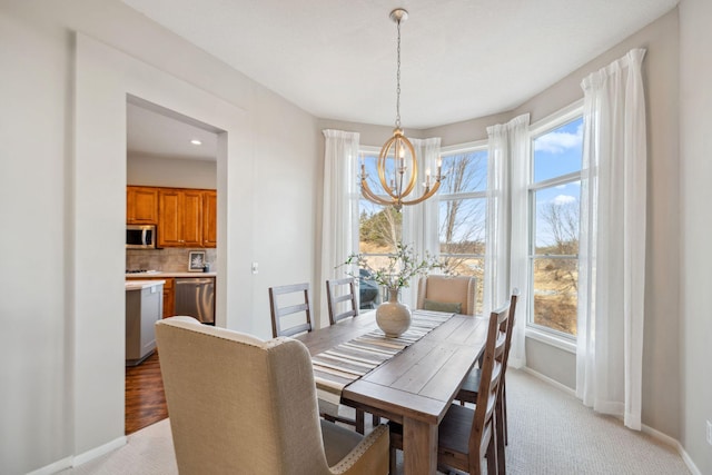 dining space with baseboards, a notable chandelier, and light carpet