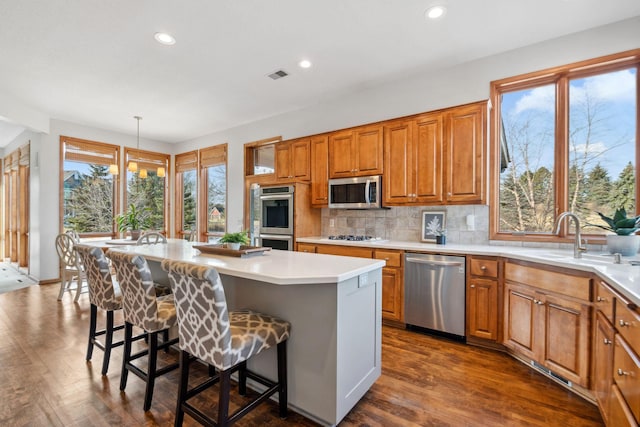 kitchen with visible vents, a sink, a kitchen breakfast bar, appliances with stainless steel finishes, and brown cabinetry