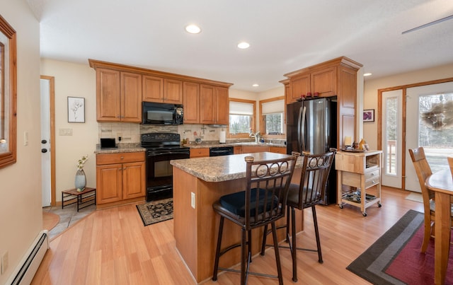 kitchen with black appliances, a sink, backsplash, light wood-style floors, and a baseboard radiator