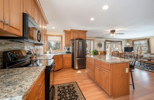 kitchen featuring light wood finished floors, black microwave, a breakfast bar area, range with electric stovetop, and freestanding refrigerator