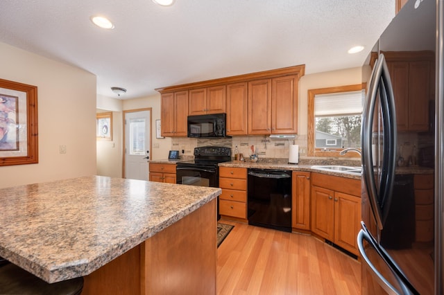 kitchen featuring black appliances, brown cabinets, light wood-type flooring, and a sink