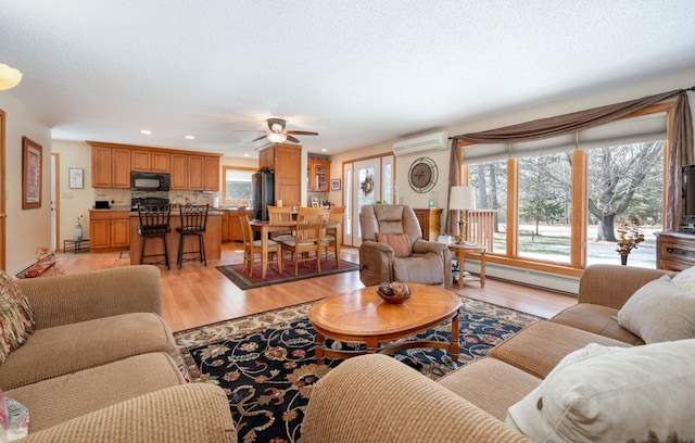 living room with a baseboard heating unit, light wood finished floors, a textured ceiling, and a wall mounted AC