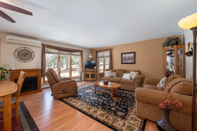 living area with a fireplace, an AC wall unit, light wood-style floors, a textured ceiling, and baseboard heating