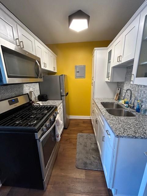 kitchen featuring a sink, glass insert cabinets, baseboards, appliances with stainless steel finishes, and dark wood-style flooring