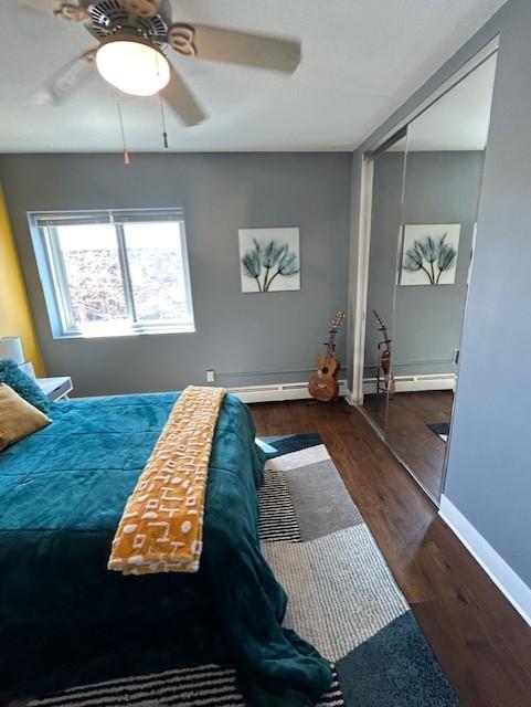 bedroom with wood finished floors, baseboards, ceiling fan, a closet, and a baseboard heating unit