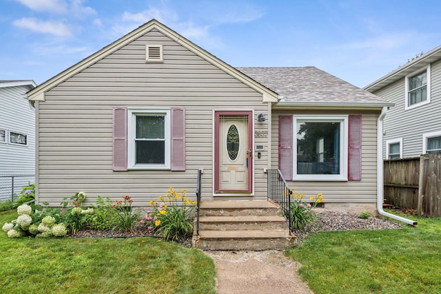 bungalow-style home with a shingled roof, a front yard, and fence