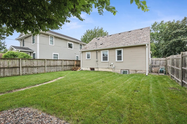 back of property with a lawn, a shingled roof, and a fenced backyard