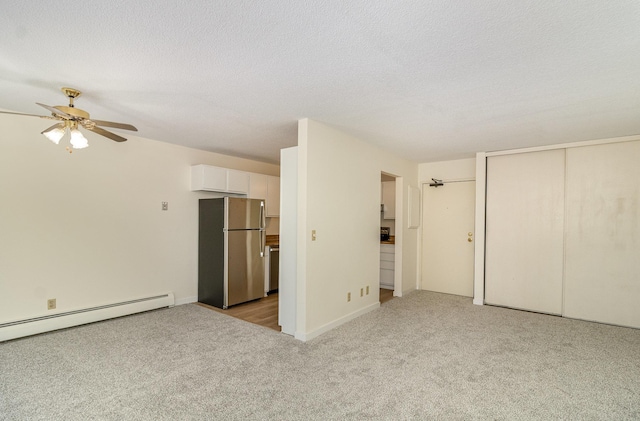 interior space with a textured ceiling, baseboard heating, freestanding refrigerator, and light carpet