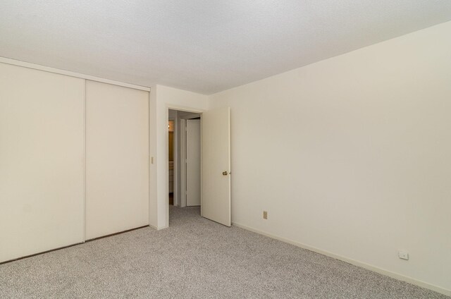 unfurnished bedroom with a textured ceiling, baseboards, a closet, and light carpet