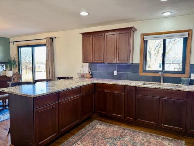 kitchen featuring tasteful backsplash, light stone counters, a peninsula, dark wood-style floors, and a sink