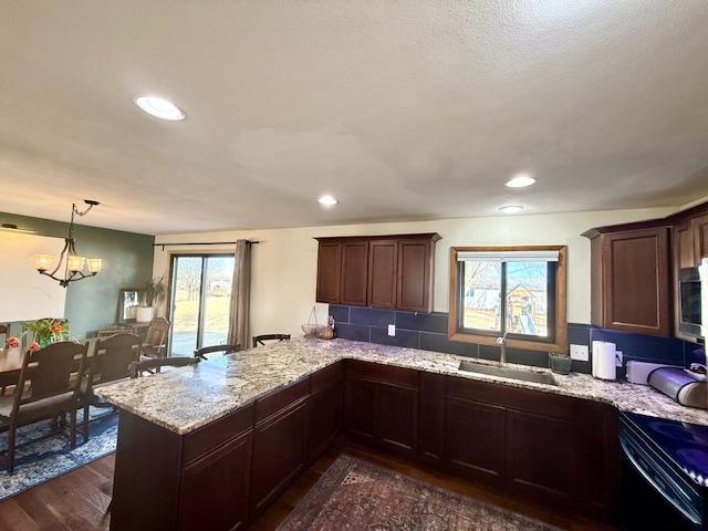 kitchen featuring dark wood-type flooring, light stone counters, a peninsula, electric range, and a sink