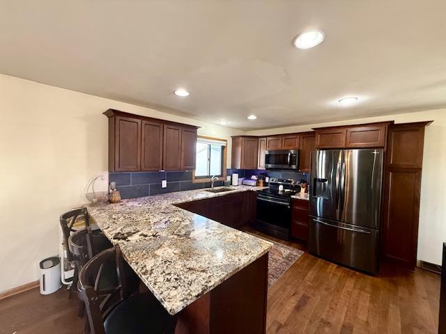 kitchen featuring light stone counters, a peninsula, dark wood-style flooring, a sink, and appliances with stainless steel finishes