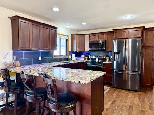 kitchen featuring light wood-type flooring, a sink, tasteful backsplash, stainless steel appliances, and a peninsula