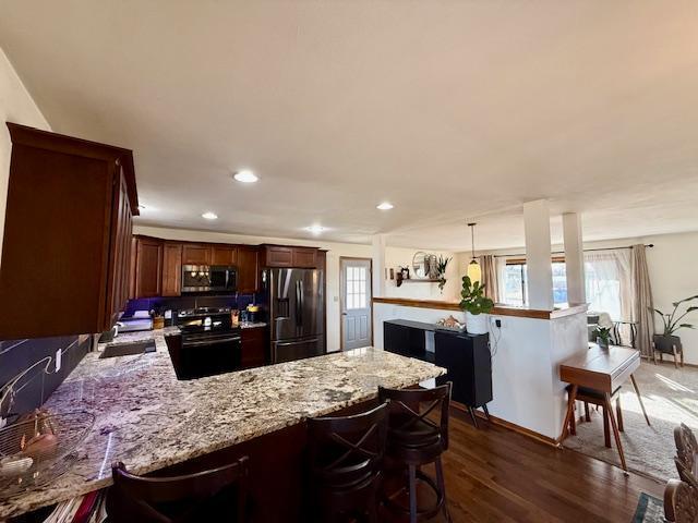 kitchen with a breakfast bar area, a peninsula, dark wood-style flooring, a sink, and stainless steel appliances