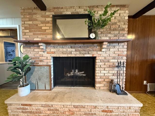 room details with beam ceiling, wooden walls, and a brick fireplace