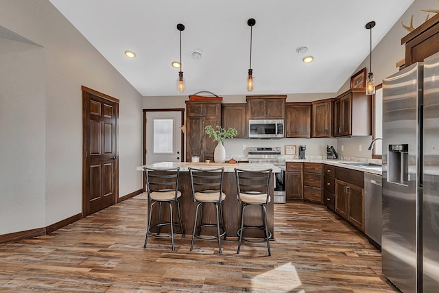 kitchen with a sink, dark wood finished floors, stainless steel appliances, light countertops, and lofted ceiling