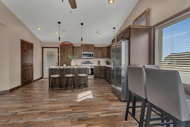 kitchen with dark wood finished floors, appliances with stainless steel finishes, a kitchen island, and lofted ceiling